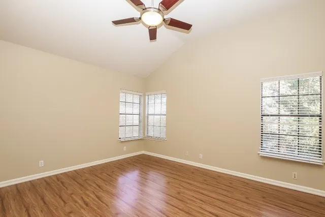 an empty room with wooden floor fan and windows