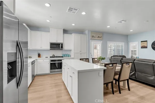 a kitchen with stainless steel appliances granite countertop a stove top oven a sink a refrigerator a dining table and chairs with wooden floor