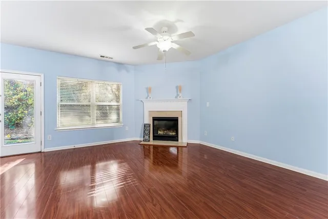 an empty room with wooden floor a chandelier fan and windows