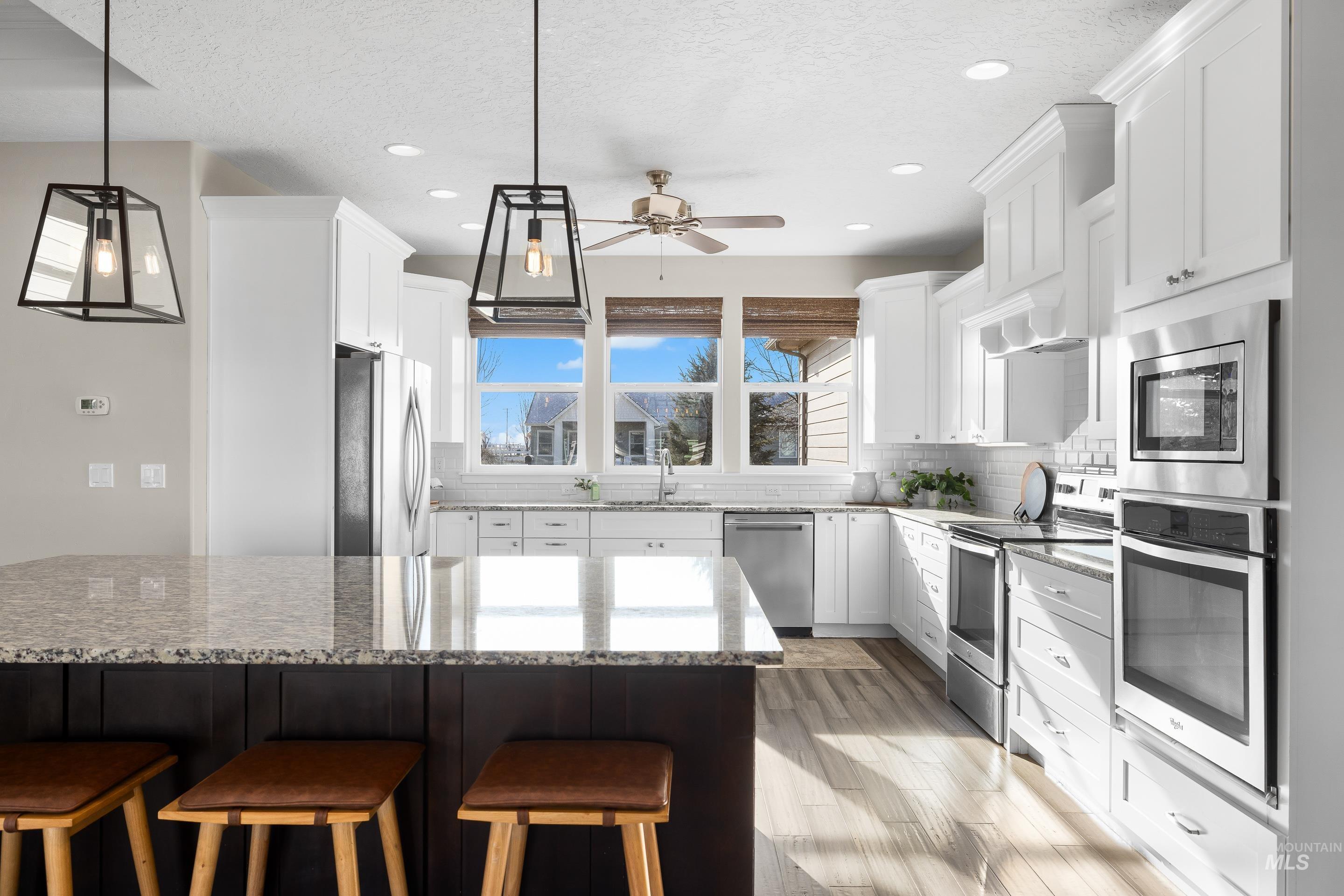 8018 Plumberry Court Middleton, ID 83644 - Photo 18 of 50 Kitchen featuring decorative light fixtures, light stone countertops, a kitchen bar, stainless steel appliances, and white cabinets