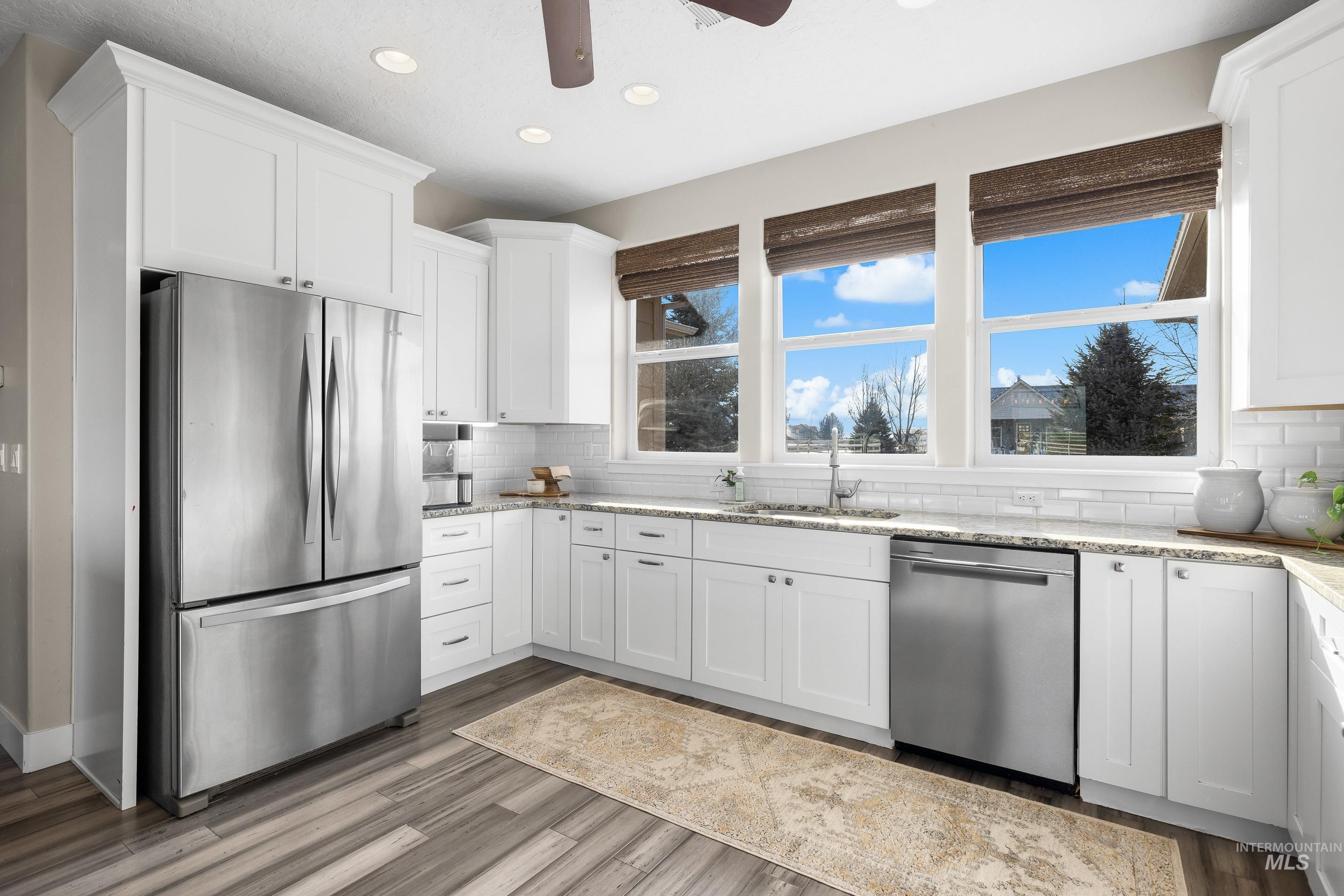 8018 Plumberry Court Middleton, ID 83644 - Photo 21 of 50 Kitchen with appliances with stainless steel finishes, white cabinets, light stone counters, ceiling fan, and dark wood-style floors