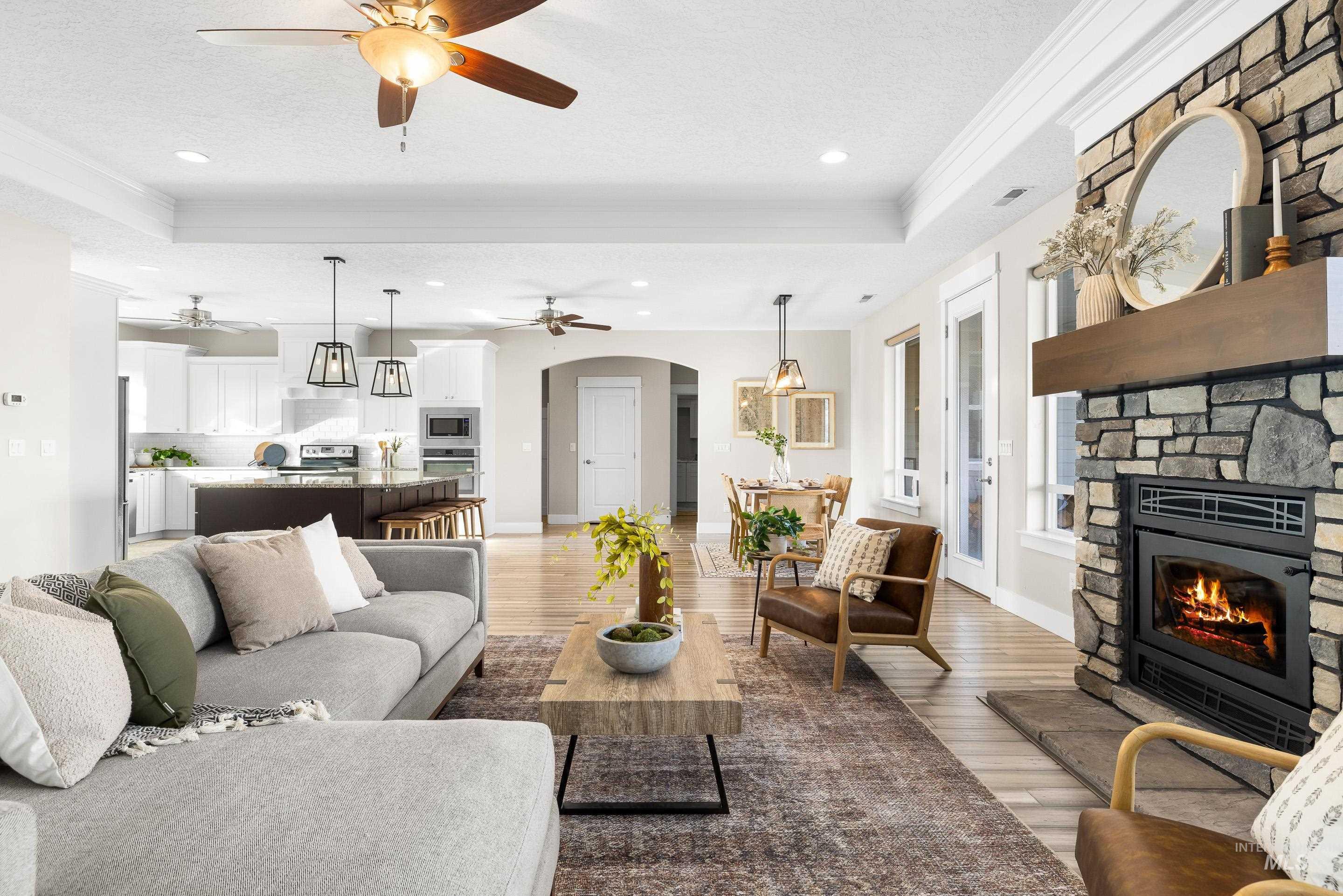 8018 Plumberry Court Middleton, ID 83644 - Photo 9 of 50 Living room featuring a textured ceiling, a stone fireplace, light wood-style floors, arched walkways, and a raised ceiling