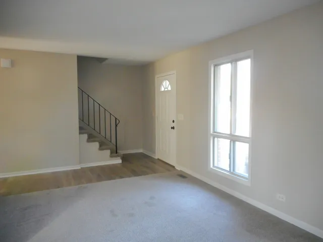a view of an empty room with wooden floor fridge and a window