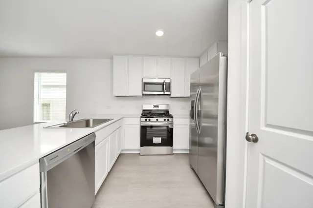 a kitchen with stainless steel appliances granite countertop a refrigerator a stove a sink and white cabinets