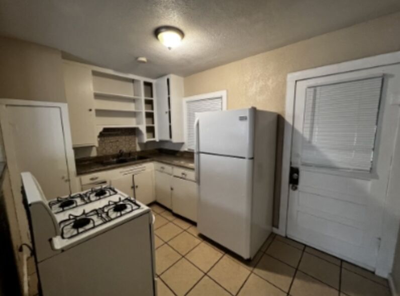 301 Cardinal Street San Marcos, TX 78666 - Photo 3 of 9 Kitchen featuring white appliances, dark countertops, open shelves, white cabinetry, and a textured ceiling