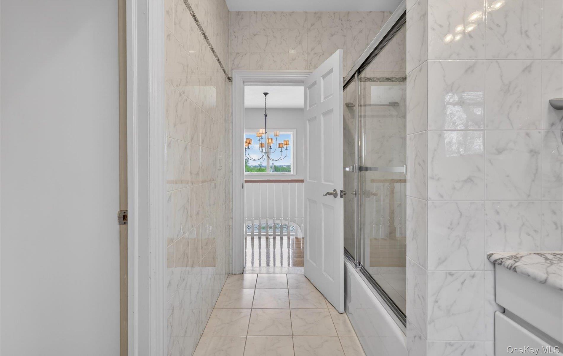 16 East Slope Road Bayville, NY 11709 - Photo 33 of 48 Bathroom featuring extensive floor-to-ceiling marble-look tiling, a glass-enclosed shower/tub combination, and a white vanity with a marble-look countertop