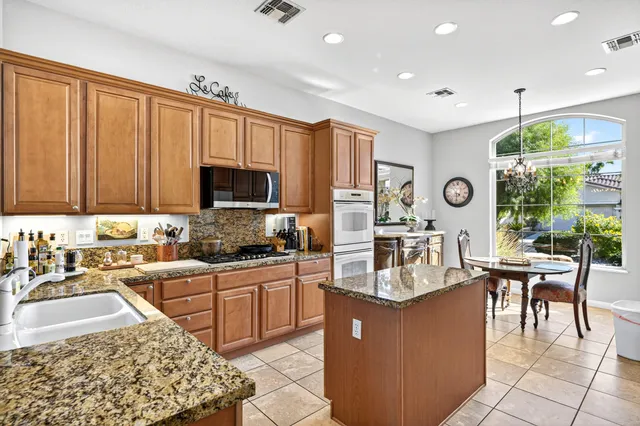 a kitchen with stainless steel appliances granite countertop a stove top oven a sink dishwasher a dining table and chairs with wooden floor