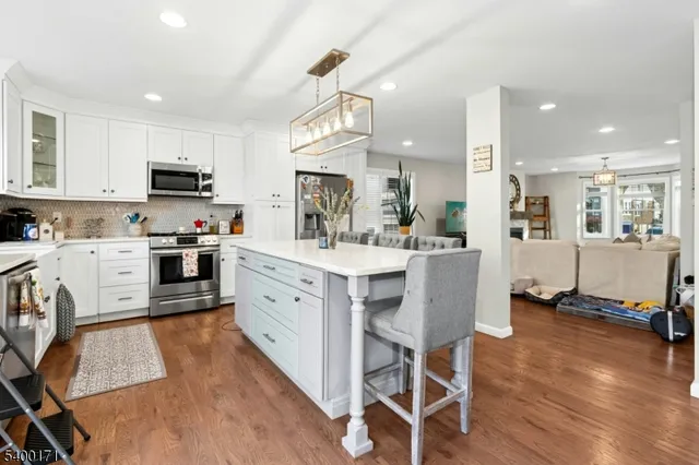 a kitchen with stainless steel appliances kitchen island granite countertop a stove top oven a sink a refrigerator white cabinets and wooden floor