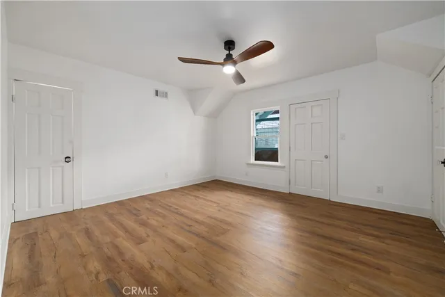 an empty room with wooden floor ceiling fan and windows