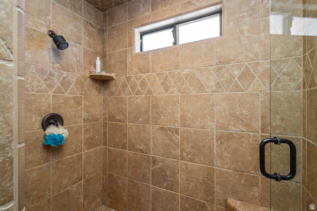 892 Cambridge Drive St. George, UT 84770 - Photo 45 of 65 Tiled shower enclosure featuring a bronze showerhead and control, a decorative tile band, a corner shelf, and a frosted window