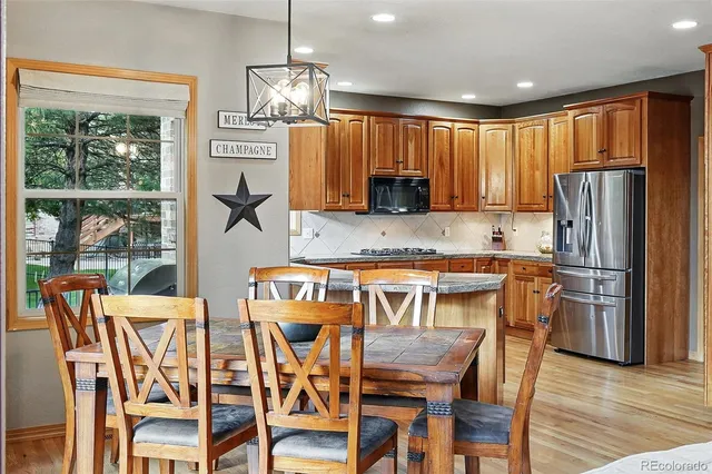 a kitchen with stainless steel appliances granite countertop a dining table chairs refrigerator and sink