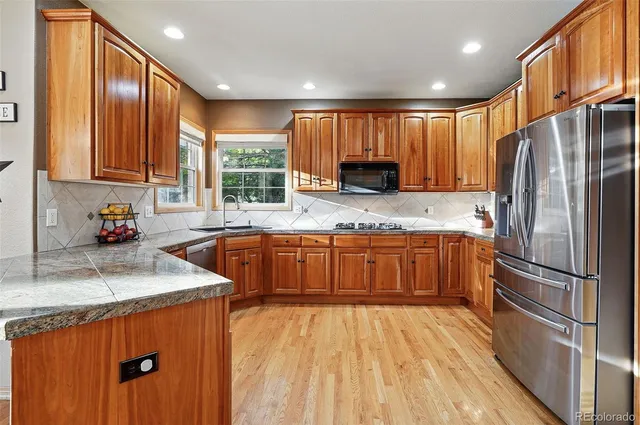 a kitchen with stainless steel appliances granite countertop a refrigerator a sink dishwasher a stove with wooden cabinets and floor