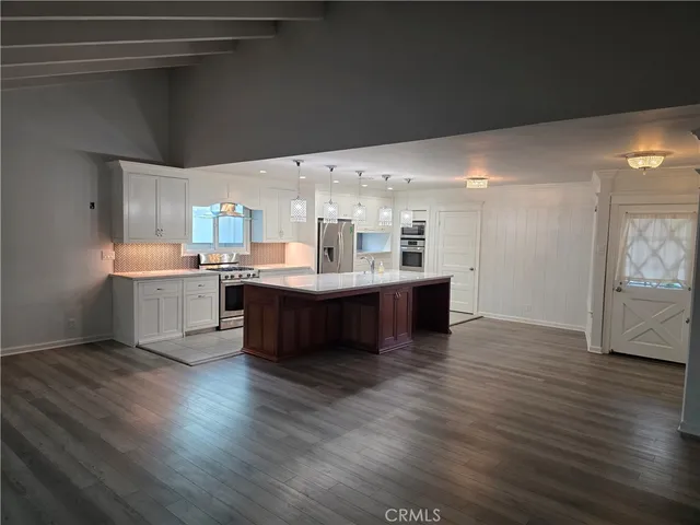 a living room with stainless steel appliances kitchen island a sink dishwasher a stove and a refrigerator with wooden floor