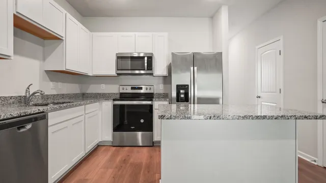 a kitchen with stainless steel appliances granite countertop a refrigerator a sink and white cabinets