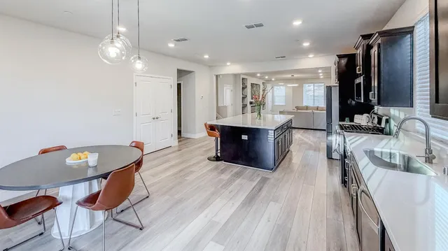 a large kitchen with kitchen island a stove a sink a refrigerator and a dining table with wooden floor