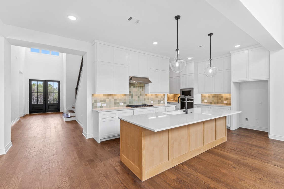 4608 Destination Way Jonestown, TX 78645 - Photo 7 of 29 a large kitchen with kitchen island a stove a sink a center island and wooden floor