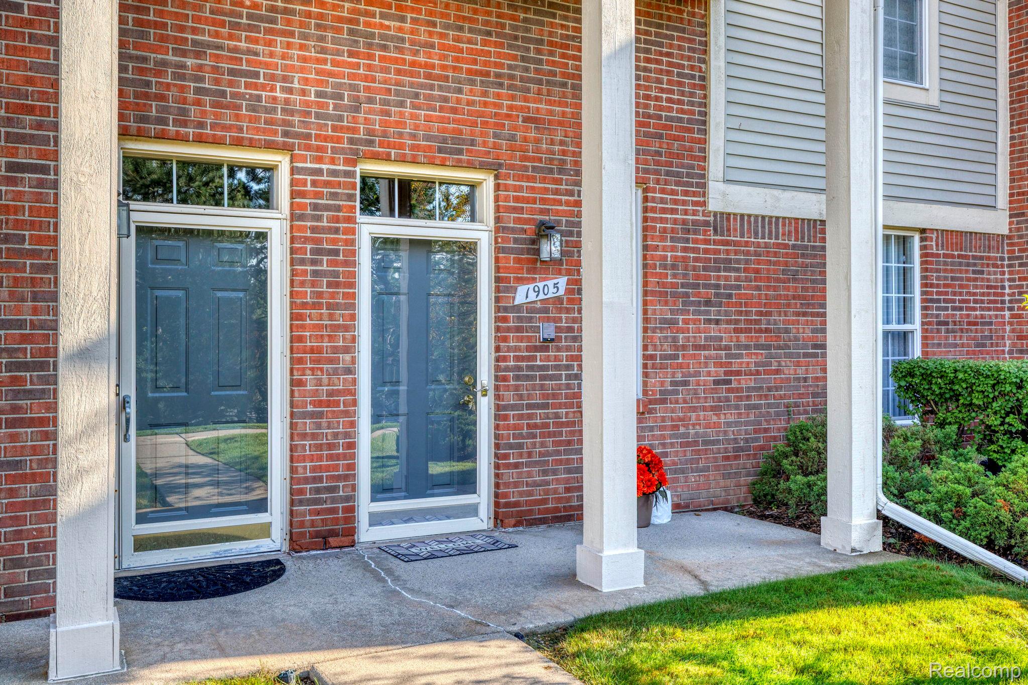 1905 Flagstone Circle Rochester, MI 48307 - Photo 3 of 33 Brick exterior facade with light gray siding accents, white trim windows, two entry doors with storm doors, and a concrete entry porch