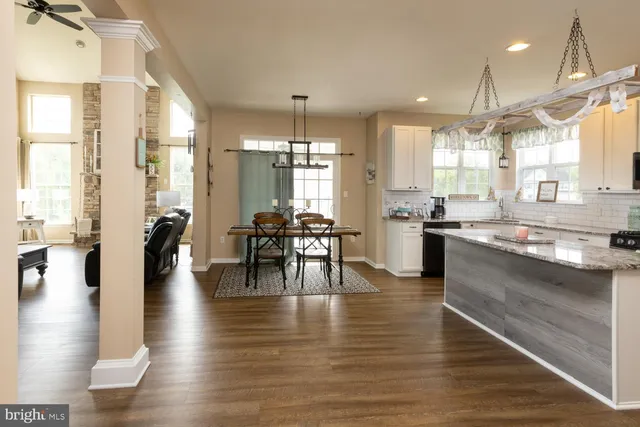 a open kitchen with granite countertop a stove a sink a dining table and chairs with wooden floor