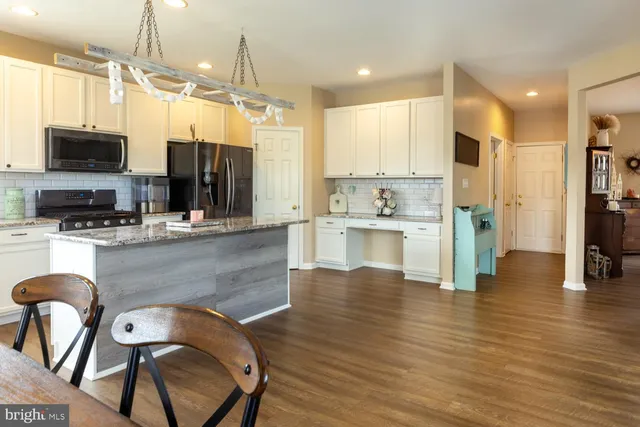 a large kitchen with stainless steel appliances kitchen island granite countertop a refrigerator a stove top oven a sink dishwasher and white cabinets with wooden floor