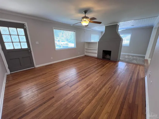 an empty room with wooden floor fireplace and windows