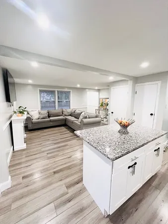 a kitchen with stainless steel appliances kitchen island granite countertop a sink dishwasher and white cabinets with wooden floor