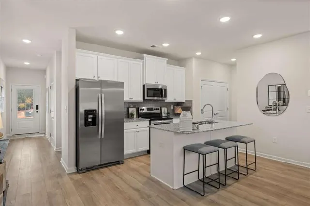 a kitchen with stainless steel appliances granite countertop a refrigerator a stove top oven a sink dishwasher a dining table and chairs with wooden floor