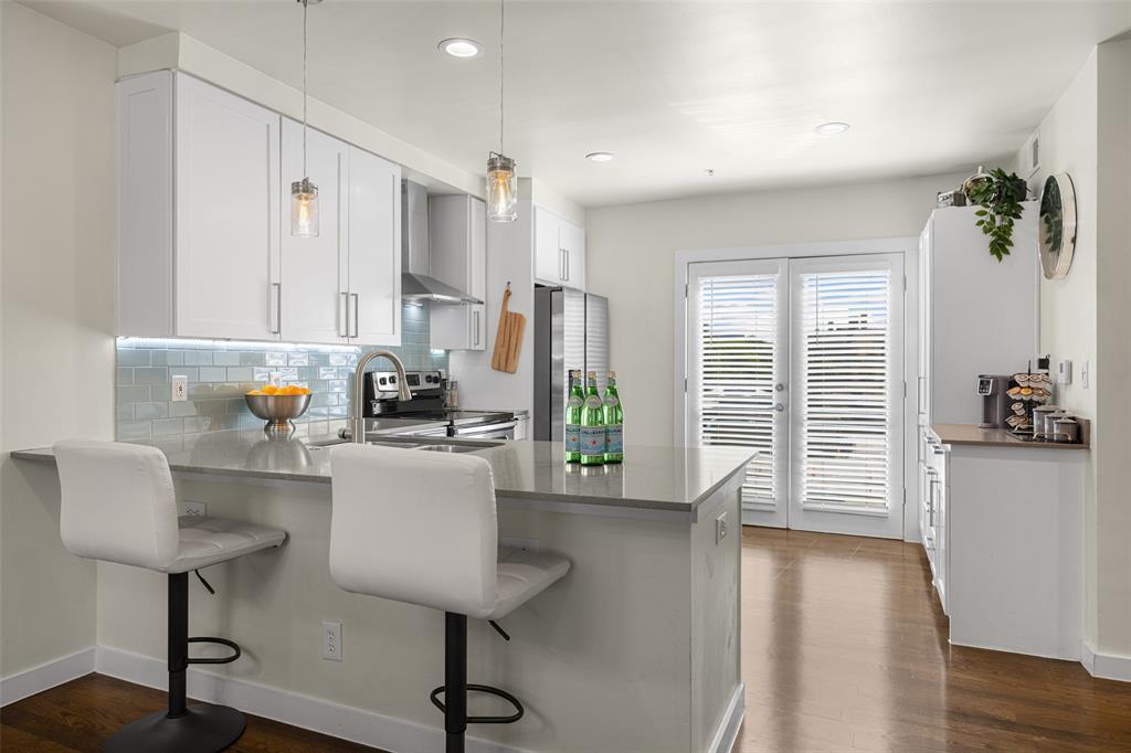 3922 Gilbert Avenue, Unit 214 Dallas, TX 75219 - Photo 1 of 27 Modern kitchen featuring white cabinetry, a light blue subway tile backsplash, a gray countertop island with seating, stainless steel appliances, and wood-finish flooring