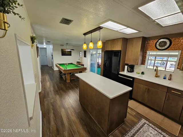 a kitchen view with stainless steel appliances a dining table chairs wooden floor and a refrigerator