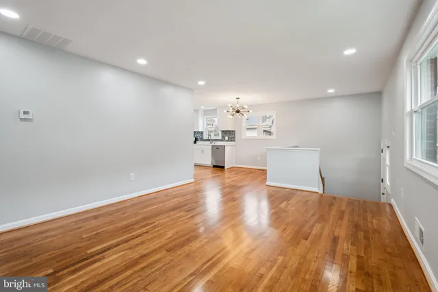 a view of a kitchen and an empty room with wooden floor