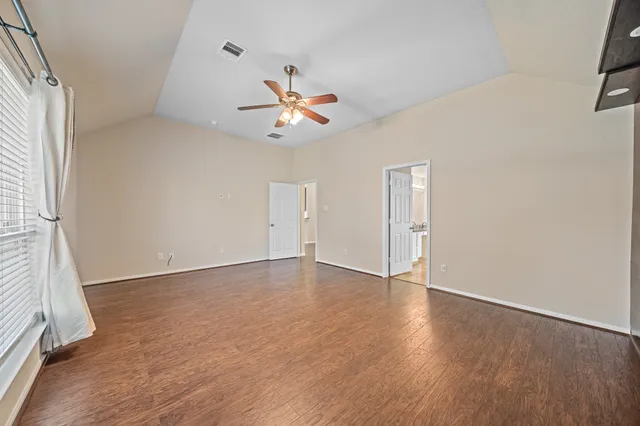 an empty room with wooden floor chandelier fan and windows