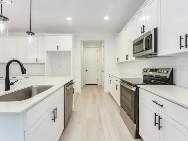 a kitchen with stainless steel appliances a sink a stove top oven a refrigerator with white cabinets and wooden floor