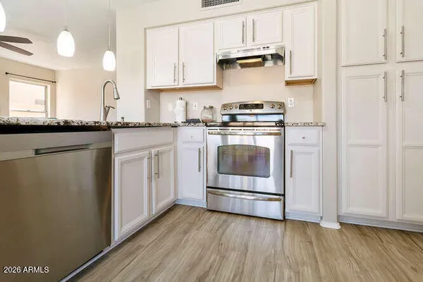 a kitchen with stainless steel appliances granite countertop a stove a sink and white cabinets with wooden floors