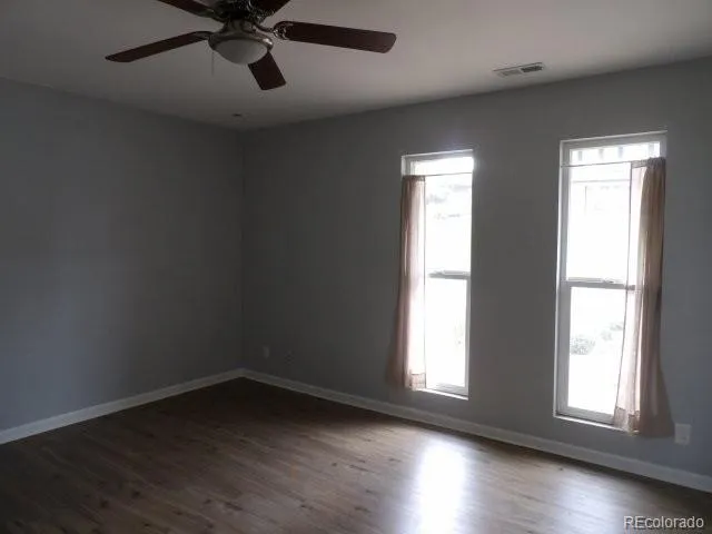 an empty room with wooden floor and windows with curtains