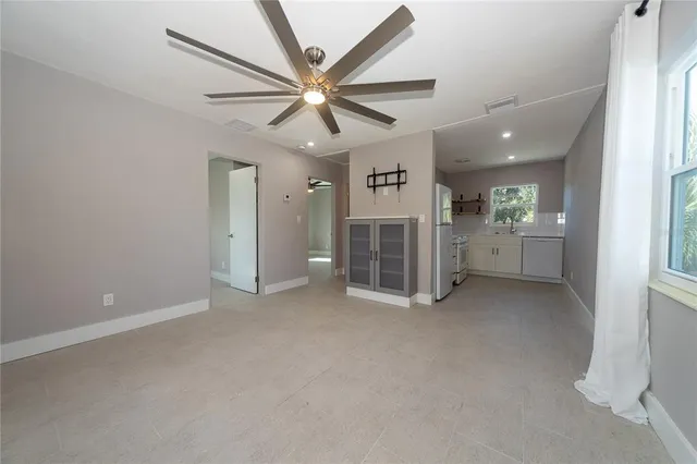 an empty room with chandelier fan and windows