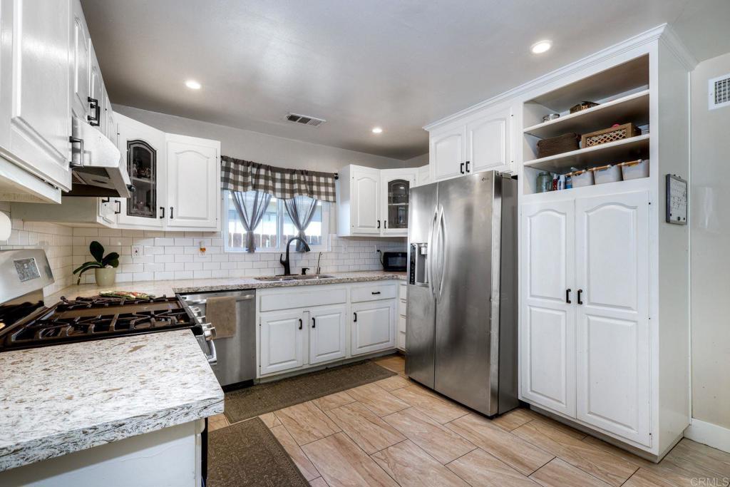 924 Daisy Street Escondido, CA 92027 - Photo 6 of 25 a kitchen with stainless steel appliances granite countertop a refrigerator a sink dishwasher and white cabinets with wooden floor