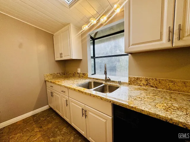 a kitchen with granite countertop a sink a stove top oven and cabinetry