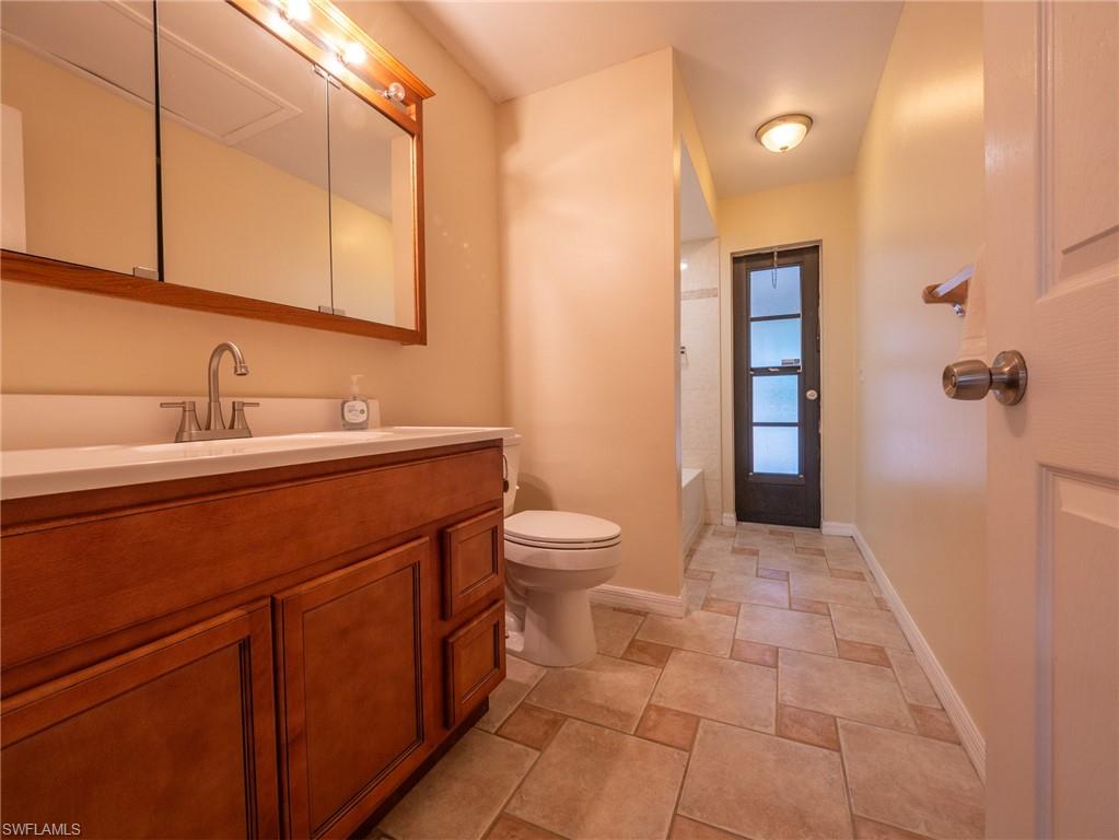18414 Tulip Road Fort Myers, FL 33967 - Photo 25 of 37 Bathroom featuring a wood-finish vanity with an integrated sink and brushed nickel faucet, a medicine cabinet with integrated lighting, a toilet, and tiled flooring