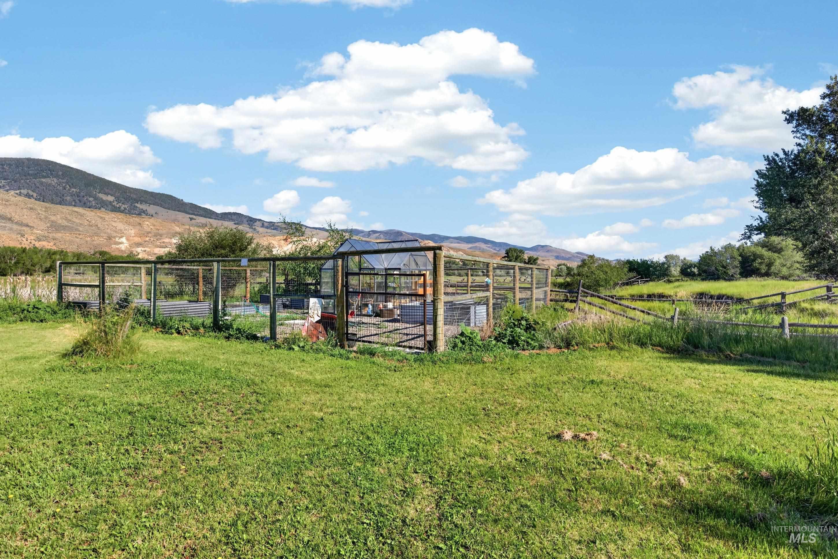 63 Mountain View Road Salmon, ID 83467 - Photo 48 of 50 Expansive grassy area featuring a fenced enclosure, a greenhouse structure, and mountain scenery