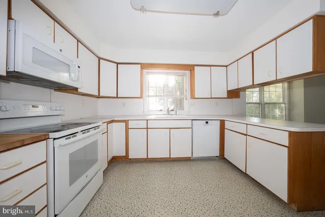 a kitchen with granite countertop white cabinets white appliances a sink and a window