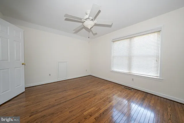 an empty room with wooden floor fan and windows