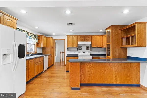 a kitchen with stainless steel appliances granite countertop a refrigerator a sink dishwasher a stove and white cabinets with wooden floor