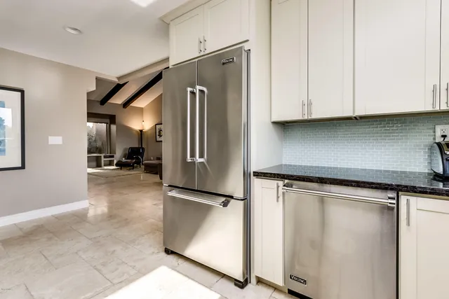 a kitchen with stainless steel appliances granite countertop a refrigerator a sink and white cabinets with wooden floor