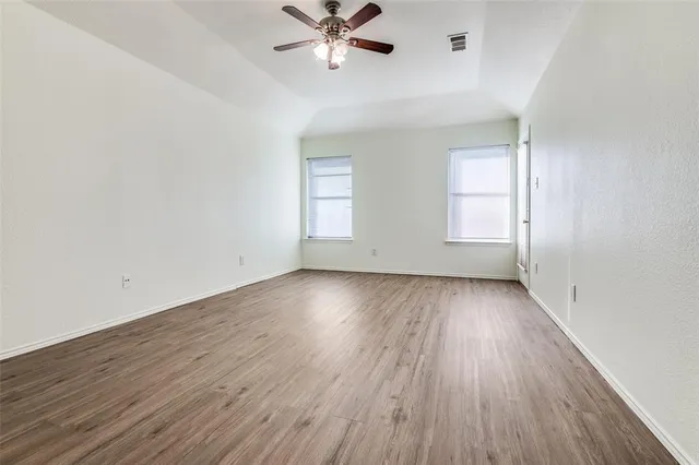 an empty room with wooden floor fan and windows