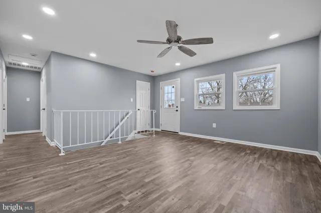 a view of an empty room with wooden floor and a ceiling fan