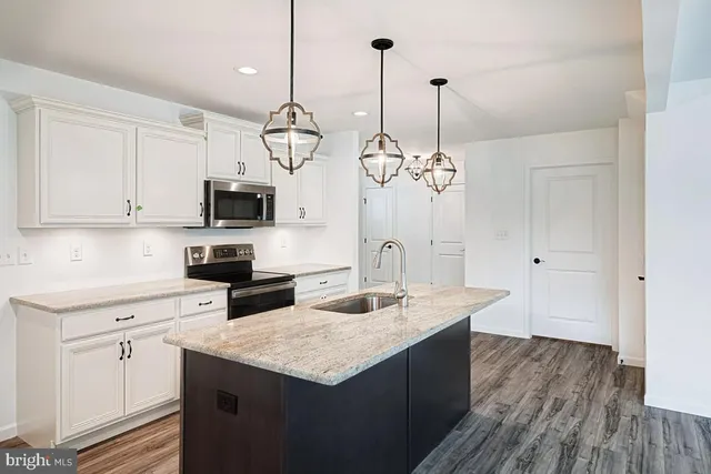 a kitchen with stainless steel appliances granite countertop a sink a microwave oven a refrigerator and white cabinets with wooden floor