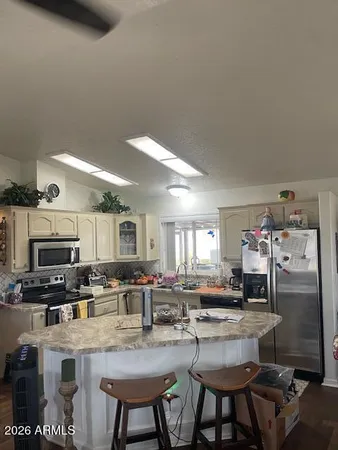 a kitchen with stainless steel appliances granite countertop a stove top oven a sink a refrigerator white cabinets and chairs