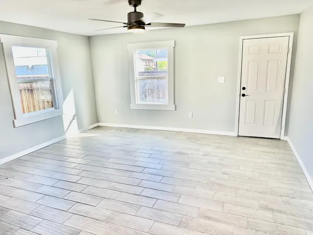an empty room with wooden floor chandelier fan and windows