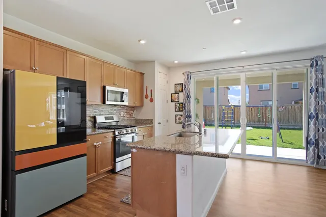 a kitchen with stainless steel appliances granite countertop a refrigerator a stove top oven and a large window with wooden floor