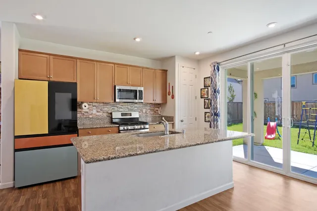 a large kitchen with stainless steel appliances granite countertop a refrigerator a stove and a wooden floor