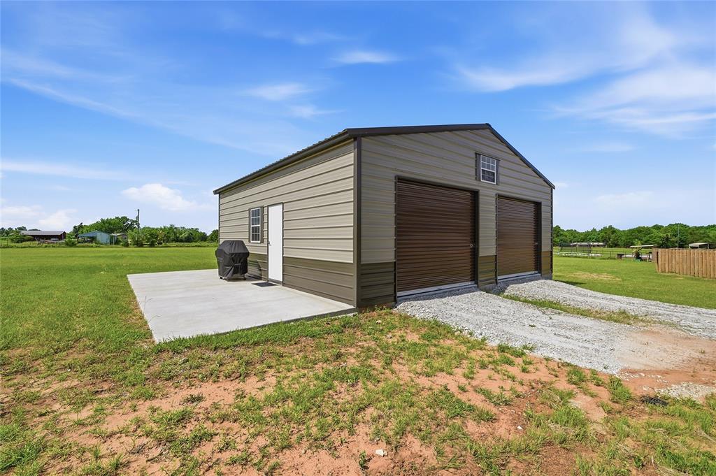 864 Shadow Valley Road Whitesboro, TX 76273 - Photo 8 of 40 Two-tone 30x30 metal outbuilding featuring two roll-up garage doors, a pedestrian entry door. Additional roll up door in the back for the lawnmower.